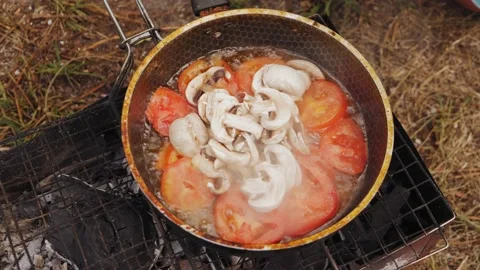 A woman's hand puts chopped champignons in a frying pan with tomatoes on the gri Stock Footage 204745892