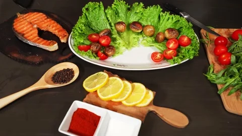 Woman's hand puts fried salmon on the plate with lettuce, potatoes Stock Footage 143567894