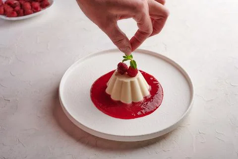 Woman's hand puts mint leaf to panna cotta with syrup and berries Stock Photos