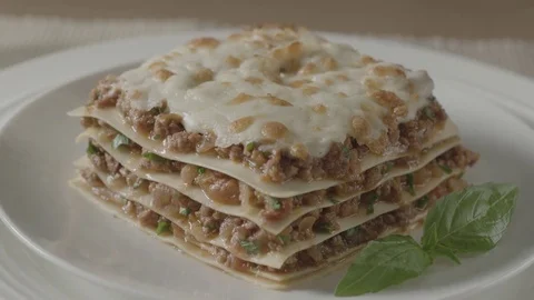 A woman's hand puts a plate on the table with a piece of tasty, meat lasagna. Video stock 83723129