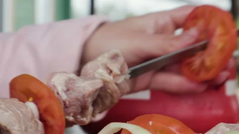 A woman's hand puts pork, tomatoes and onions on a chrome-plated grill skewer Vídeos de archivo 113667382