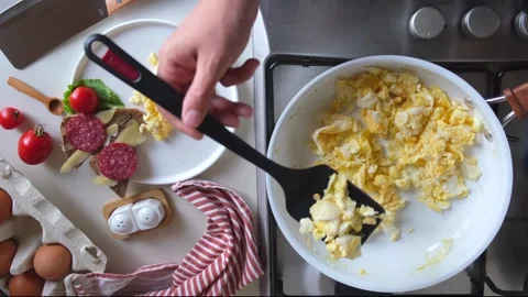 A woman's hand puts scrambled eggs from a frying pan into a white plate with Stock Footage 254550167