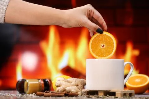 A woman's hand puts a slice of orange into white tea cup with lemon, ginger Stock Photos