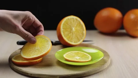 A woman's hand puts the sliced orange slices into a plate. Stockbeeldmateriaal 150697489