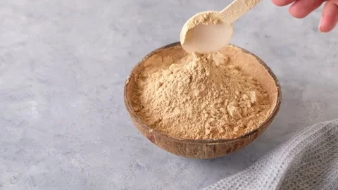 Woman's hand puts a spoon of raw maca root powder in a bowl on neutral grey Stock Footage 242667381