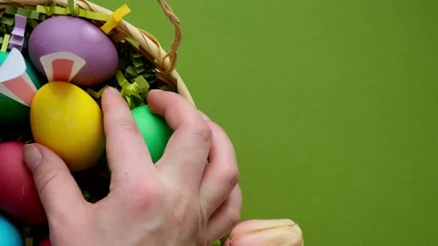 A woman's hand puts a yellow Easter egg with rabbit ears in the basket Stock Footage 235811369