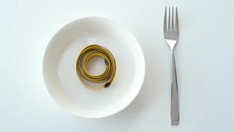 A womans hand puts a yellow measuring tape on white empty plate on the table Stock Footage 336170150