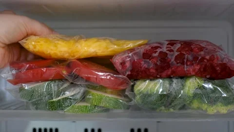 A woman's hand puts zip lock bag with yellow carrots into the refrigerator Stockbeeldmateriaal 340956819