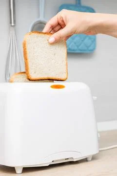 Woman's hand putting bread into the toaster. Stock Photos