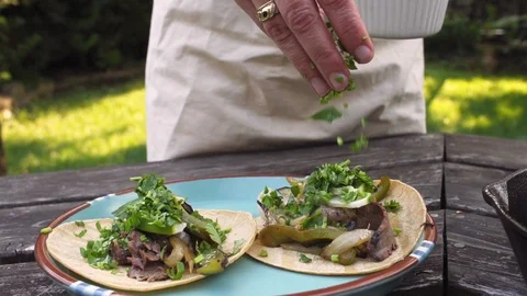 Woman's hand putting cilantro on tacos