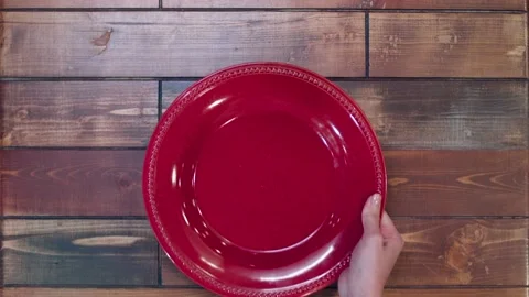 Woman's hand putting on the red plate on a wooden table Stock Footage 137225973