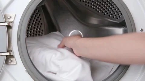 Womans hand putting white bed linen into washing machine Stock Footage 310315376