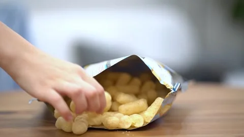 Woman's hand reaches into an open bag of crunchy corn cheese puffs Stock-Footage 342192222