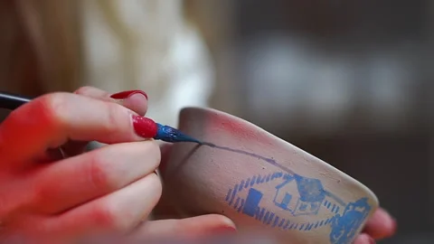 A woman's hand with red nails paints a ceramic bowl with a blue thin brush Stock Footage 256325258