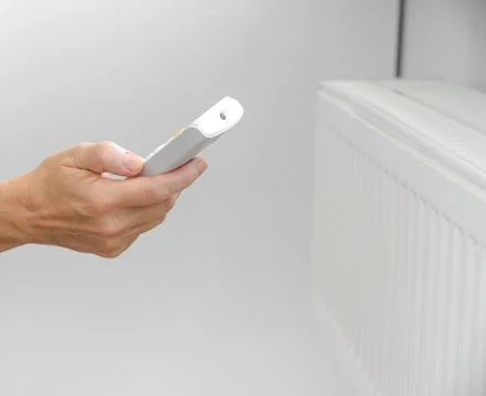 Woman's hand with a remote control from the central heating. Energy crisis. P Stock Photos