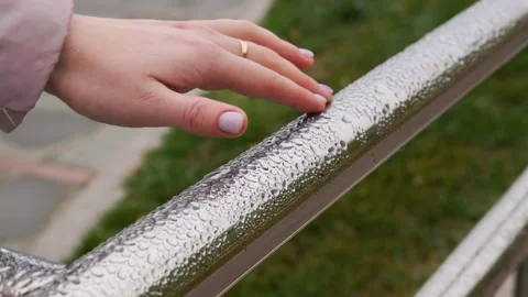 A woman's hand with a ring runs her fingers along a wet steel railing with drops Stockbeeldmateriaal 254115801