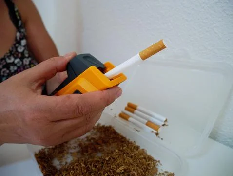 Woman's Hand with Rolling Machine and Finished Cigarettes, Homemade Smoking Fotos Stock