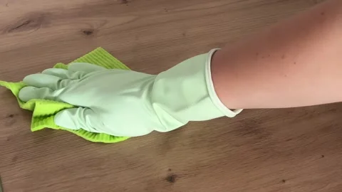 A womans hand in a rubber glove cleans a wooden table with a household rag Stock Footage 308930261