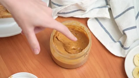 A woman's hand scoops up a peanut butter with her finger. Sweet nut butter Stock Footage
