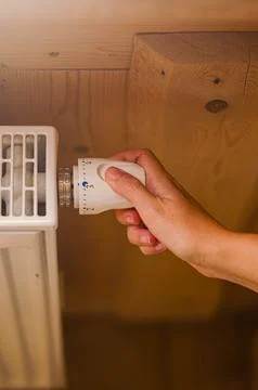 A woman's hand setting the room temperature By Thermostat in wooden house Stock Photos
