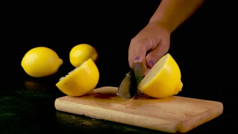 A woman's hand with a sharp knife cuts a lemon on a black background Stock Footage 203907219