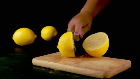 A woman's hand with a sharp knife cuts a lemon on a black background 库存影片 204745947