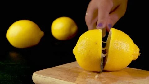 A woman's hand with a sharp knife instantly cuts a lemon on a black background Stock Footage 205392938