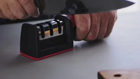 A woman's hand sharpens a kitchen knife in a special knife sharpener on the Vidéo 255801189
