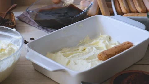 A woman's hand soaks a cookie in coffee and puts it on a tray to make a tiramisu Stock Footage 235060703