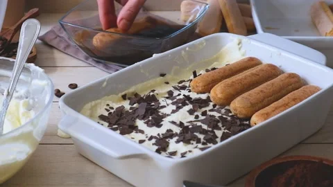 A woman's hand soaks a cookie in coffee and puts it on a tray to make a tiramisu Stock Footage 235060757