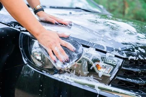 A woman's hand with a sponge washes the headlight of a car, close-up Stock Photos