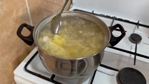 A woman's hand with a spoon interferes with the soup being prepared on the gas Stock Footage 255040806