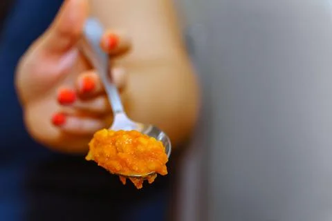 A woman's hand with a spoon in which pumpkin porridge is orange. Towards the Stock Photos