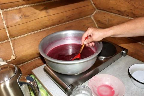 A womans hand stirs redcurrant jam in a basin on an electric hot plate Stock Photos