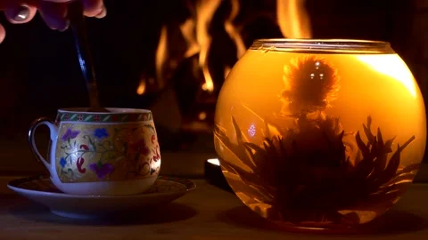 A woman's hand stirs a teaspoon of tea in a cup next to a brewed Chinese tea . Video stock 148600649