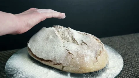The woman's hand strokes the bread, which is sprinkled with flour, on a black ba Stock Footage 89618262