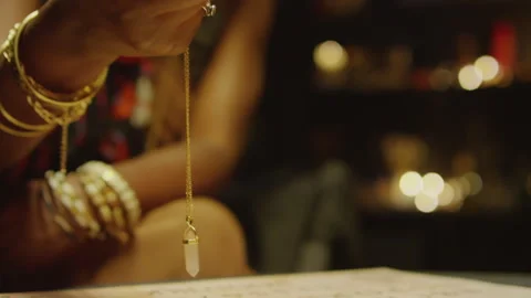 Womans Hand Swinging Pendulum on Chain over Paper with Letters Stock Footage 247638327