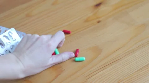 A woman's hand takes a bunch of multi-colored pills from the table. Pills are Stock Footage 262422577