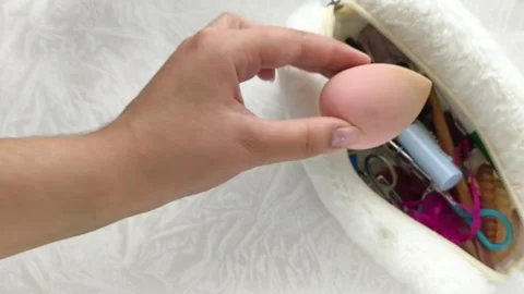 A womans hand takes a sponge from a makeup bag on the table and brings it to the Stock Footage 316286765