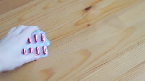 A woman's hand takes two strips of pills from the table. Taking medications. Stock Footage 262422392