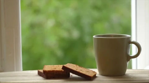 Woman's hand taking a cup of hot tea with steam for breakfast, it is raining and Stock Footage 255788626
