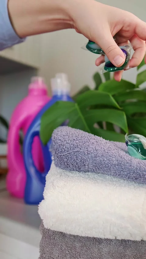 A woman's hand throws washing capsules onto a stack of towels, detergent and fab Stock Footage 295286180