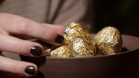 Woman's hand touches the round tea balls in gold foil in a bowl Stock Footage 97828014