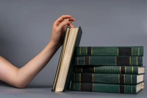 A woman's hand touches a stack of old books on a plain background Foto stock