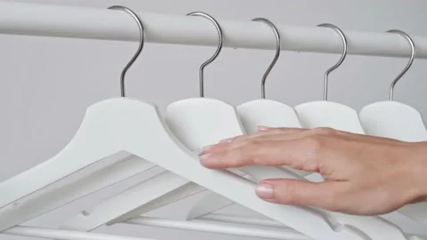 Woman's hand touches white empty wooden clothes hangers on white wall background Видео 196893366