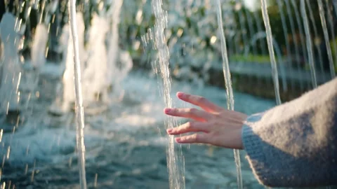 A woman's hand touching a stream of water from fountain on summer evening Stock Footage 285314265