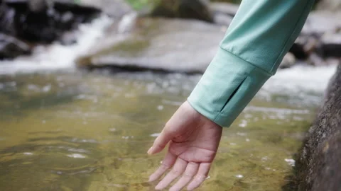 A woman's hand touching the surface of river and waterfalls. Video stock 215926393