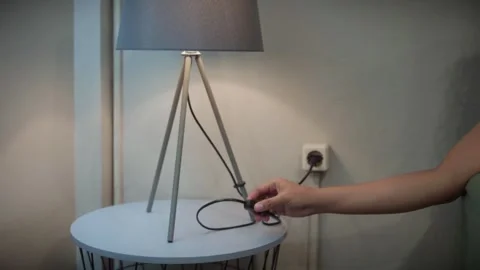 Woman's Hand Turning On Modern Tripod Table Lamp on White Side Table Video stock 346159572
