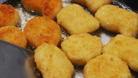 A woman's hand turns nuggets over with a spatula onto a frying pan with oil. Stock Footage 295430596