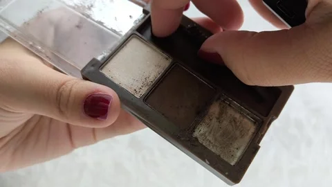A womans hand uses a brush to take brown eye shadow from a palette with brown Stock Footage 314305641